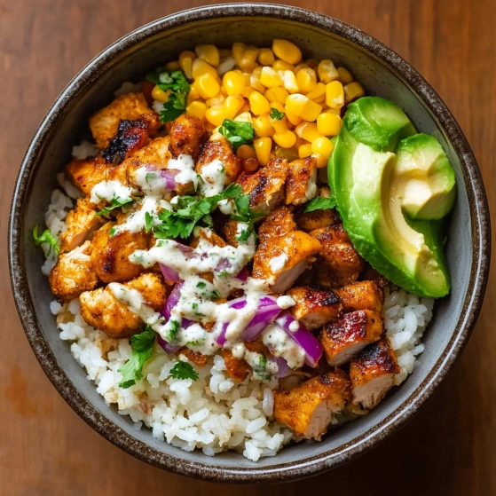 A bowl of food with rice, chicken, corn, and avocado.