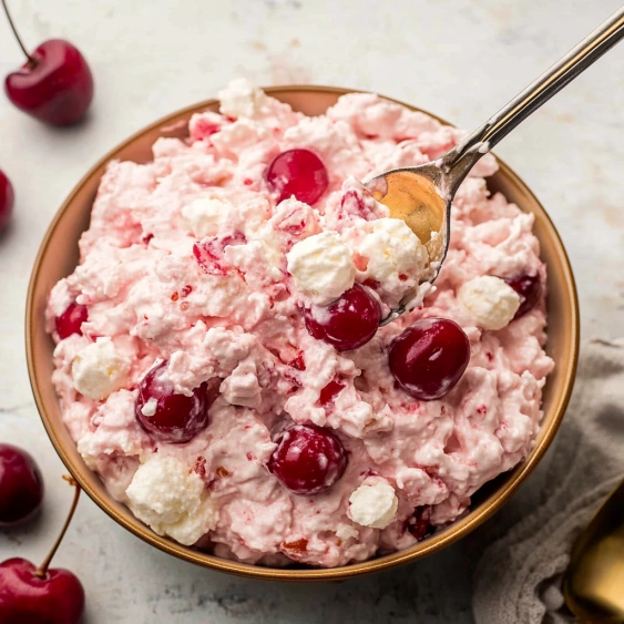 A bowl of pink dessert with cherries on top.