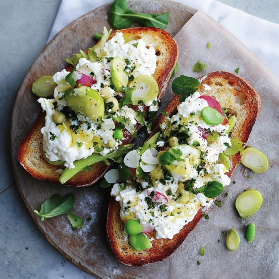 Two slices of bread with white cheese and green vegetables.