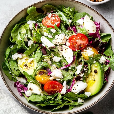 A bowl of salad with tomatoes, lettuce, and avocado.